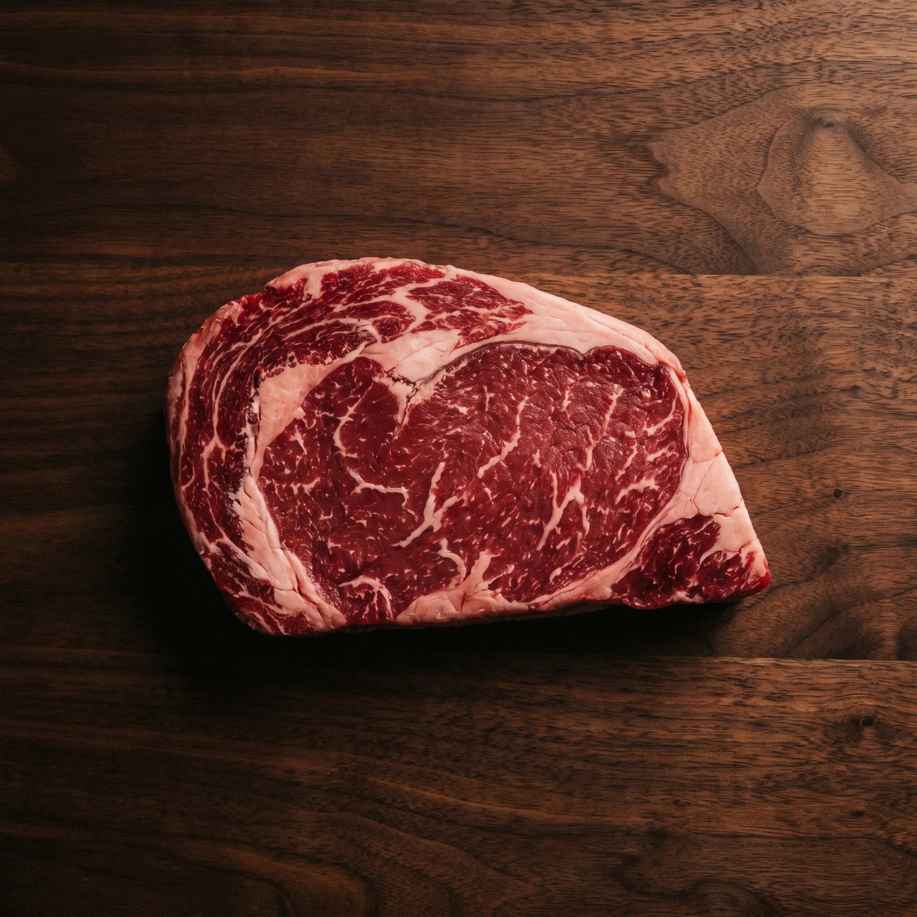 Rohes Grass-Fed Ribeye von oben auf dunklem Nussbaum